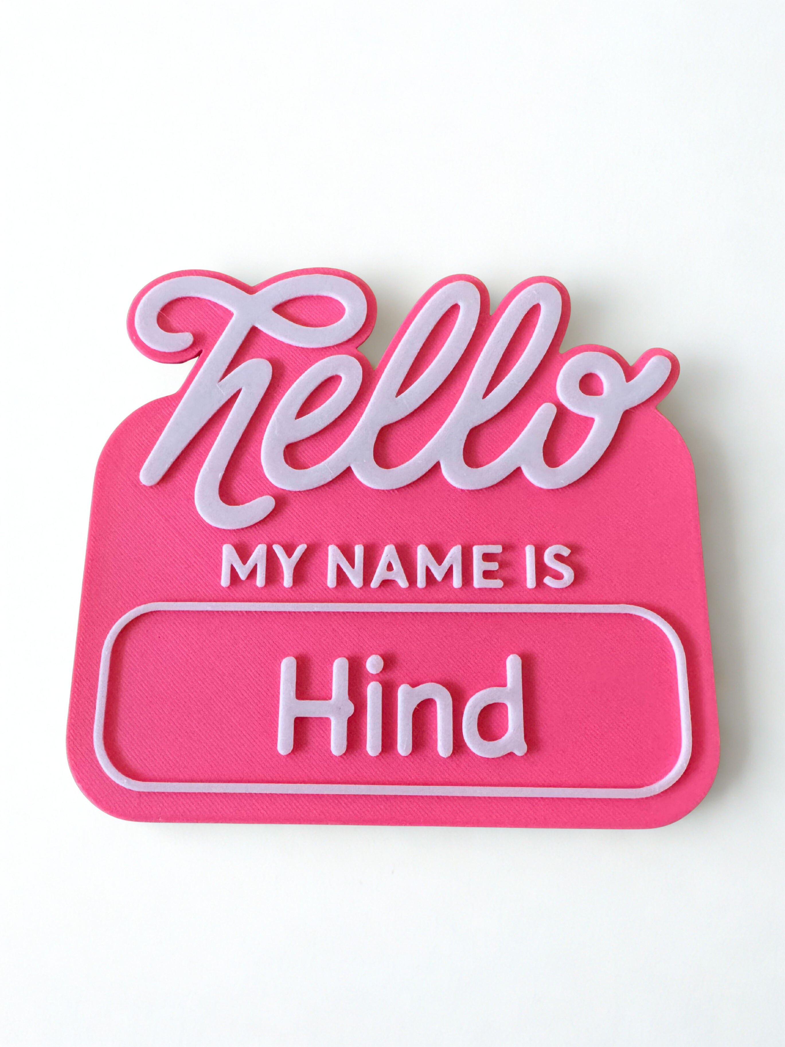 Pink name tag with 'Hello My Name is Hind' text on a white background