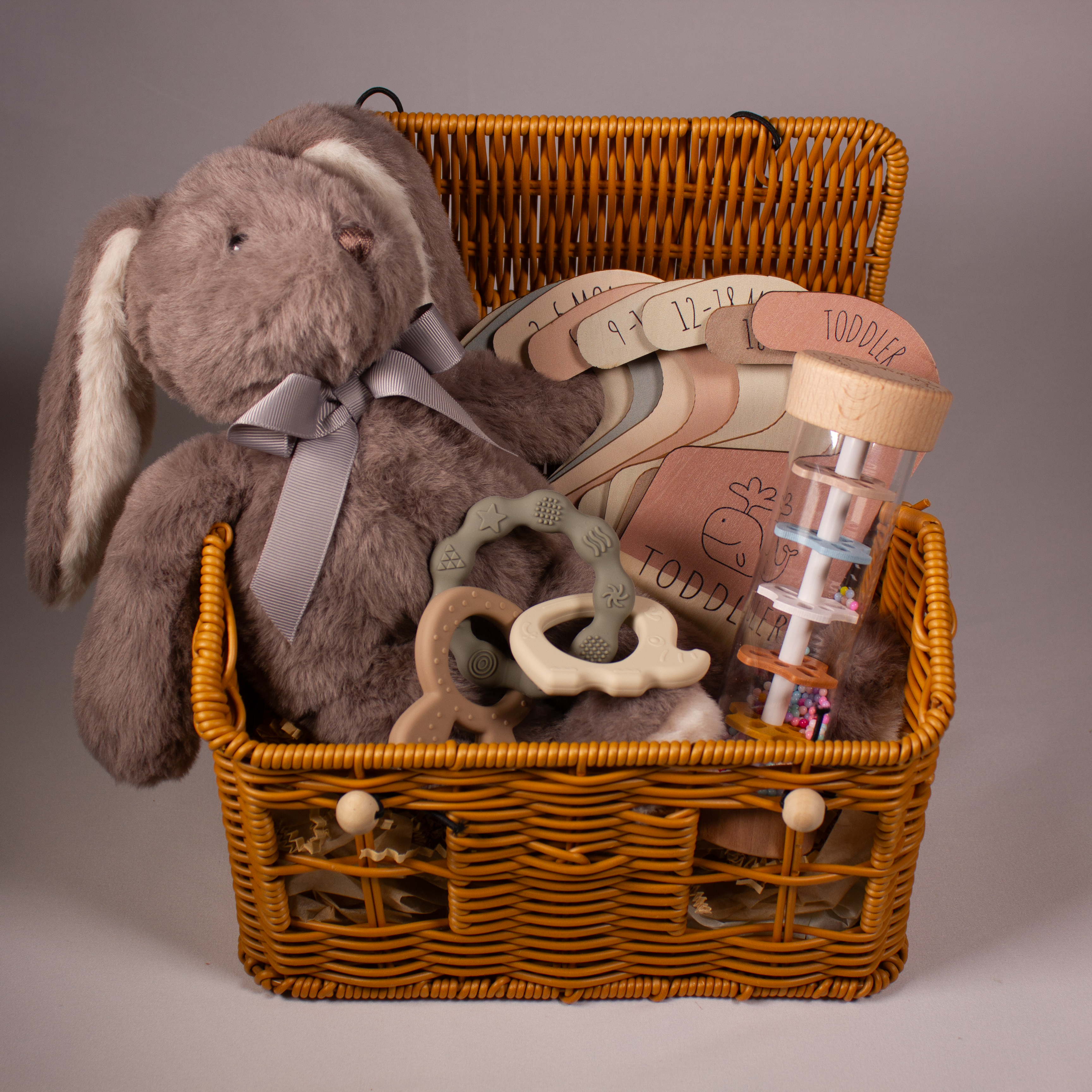 Baby gift wicker basket with plush rabbit toy, baby teether, montessori rain tube and monthly baby milestone hangers.
