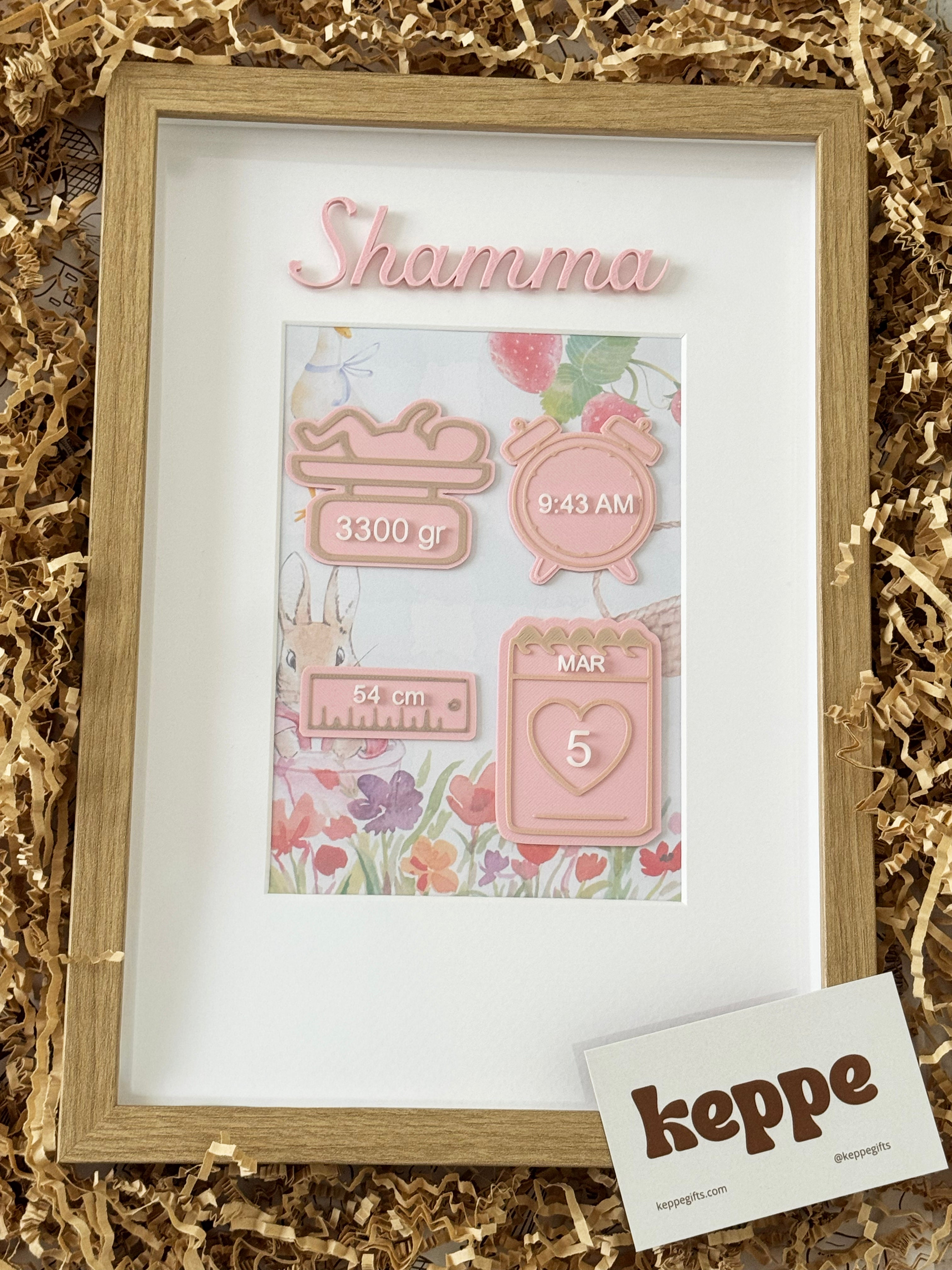 Framed baby milestone cards with 'Shenmum' branding on a gold shredded paper background